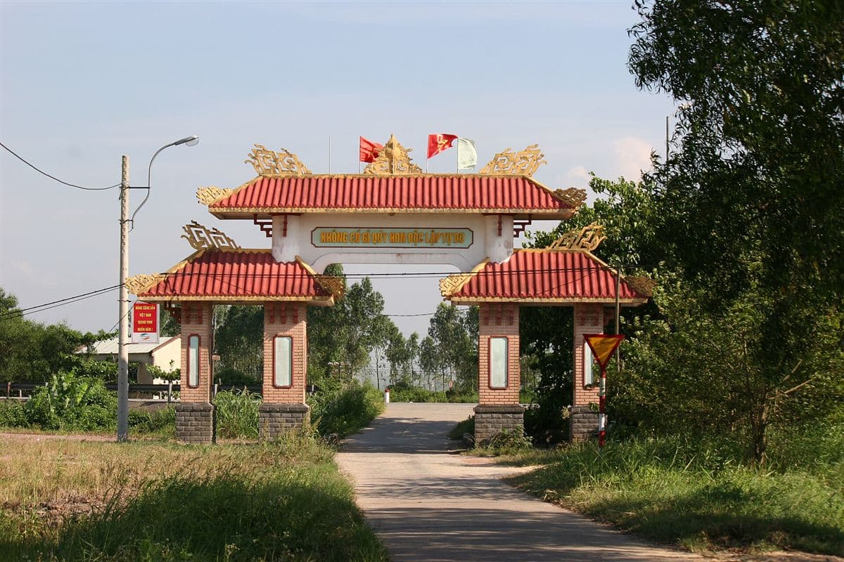 Cổng làng mái ngói đỏ, con đường bê tông dẫn vào làng giữa hàng cây xanh